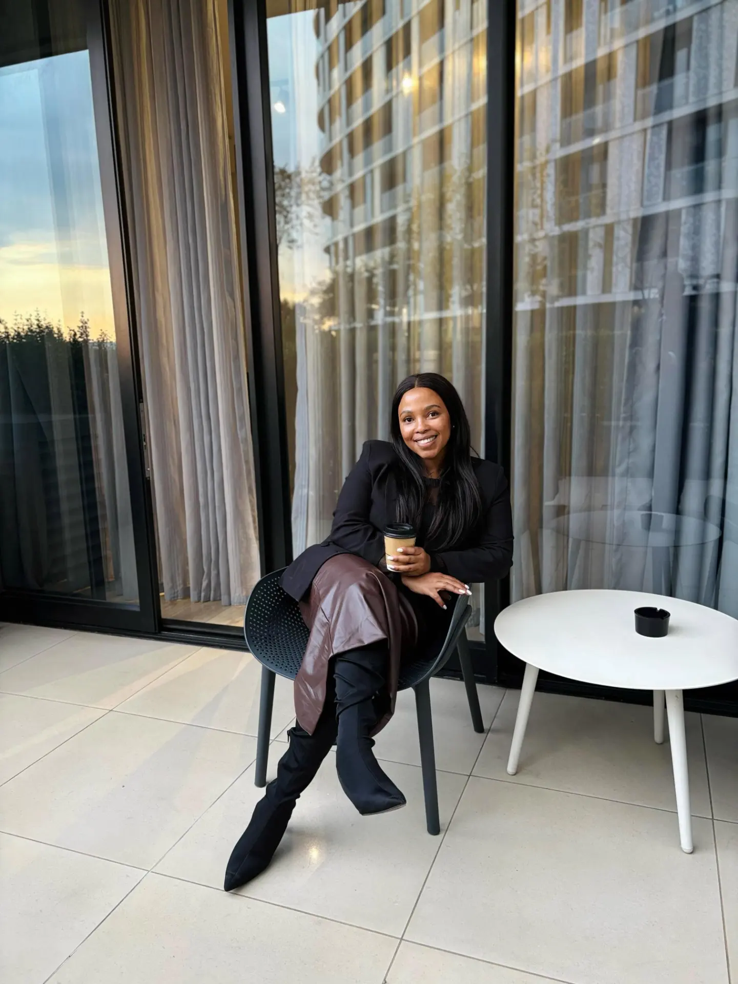 Nandisa seated with a coffee beside floor-to-ceiling windows